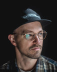 Man wearing a black cap and round glasses against a dark background
