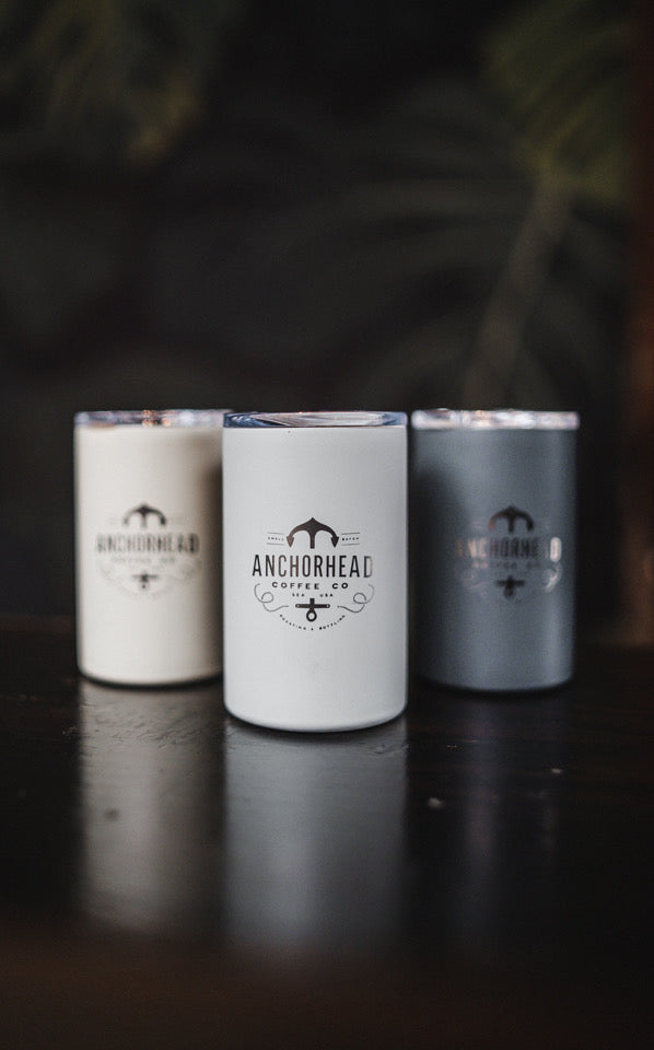 Three ceramic travel mugs with the Atlantis brand logo, in white, black, and silver colors, displayed on a dark background.